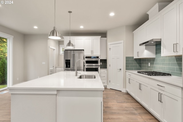 kitchen with white cabinets, appliances with stainless steel finishes, decorative light fixtures, and an island with sink