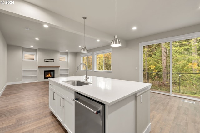 kitchen with sink, hanging light fixtures, stainless steel dishwasher, a center island with sink, and white cabinets