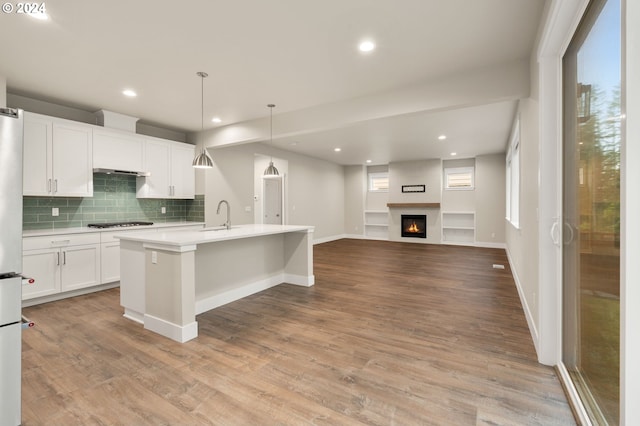 kitchen with white cabinetry, hanging light fixtures, tasteful backsplash, a center island with sink, and light wood-type flooring