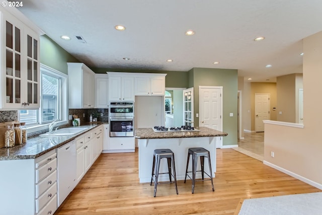 kitchen with sink, white appliances, a kitchen island, light hardwood / wood-style flooring, and white cabinetry