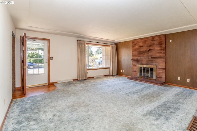 unfurnished living room with plenty of natural light, carpet, a fireplace, and wooden walls