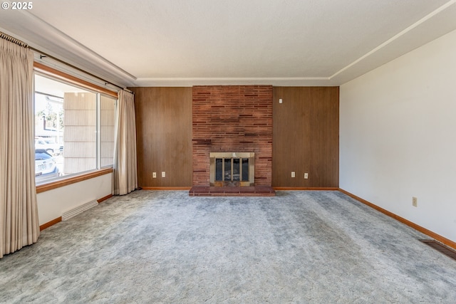 unfurnished living room featuring wooden walls, baseboards, visible vents, carpet flooring, and a brick fireplace