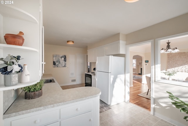 kitchen with stove, an inviting chandelier, white refrigerator, hanging light fixtures, and white cabinetry