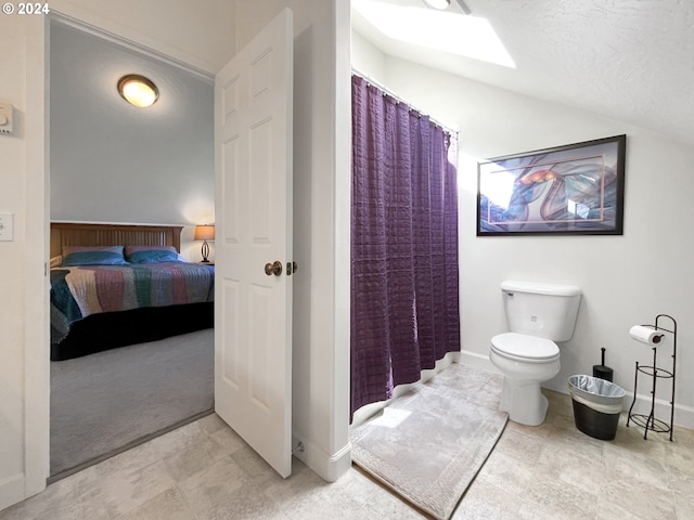 bathroom with a textured ceiling, toilet, walk in shower, and vaulted ceiling with skylight