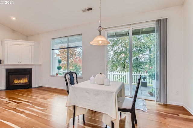 dining room with a wealth of natural light, vaulted ceiling, and light hardwood / wood-style flooring