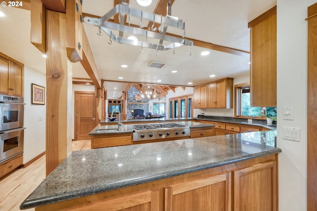 kitchen featuring sink, dark stone counters, a large fireplace, kitchen peninsula, and stainless steel appliances