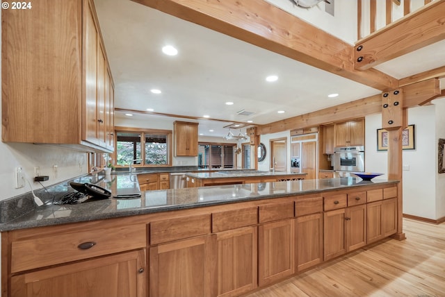 kitchen with dark stone countertops, kitchen peninsula, appliances with stainless steel finishes, and light wood-type flooring