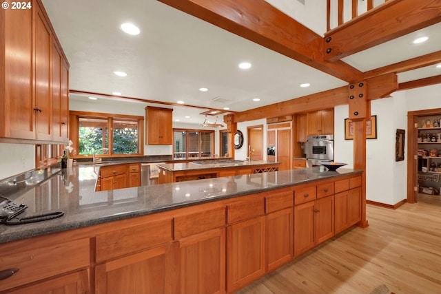 kitchen with light hardwood / wood-style flooring, dark stone countertops, beam ceiling, stainless steel appliances, and kitchen peninsula