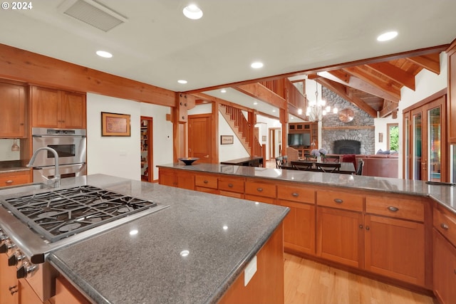 kitchen with stainless steel appliances, a center island, a fireplace, lofted ceiling with beams, and light wood-type flooring