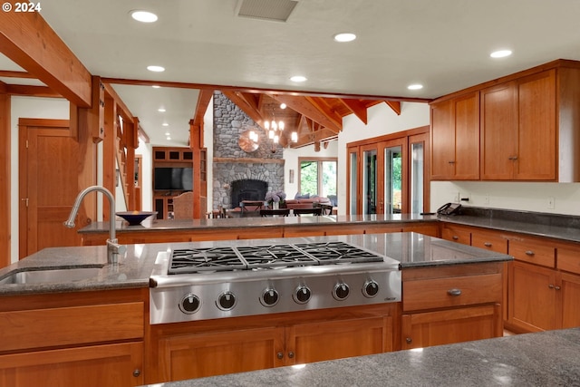 kitchen featuring lofted ceiling with beams, stainless steel gas cooktop, dark stone counters, and sink