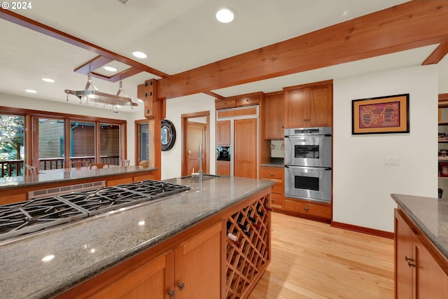 kitchen featuring appliances with stainless steel finishes, pendant lighting, dark stone counters, light hardwood / wood-style floors, and beam ceiling