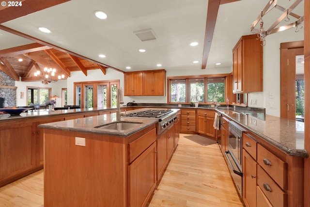 kitchen featuring appliances with stainless steel finishes, a wealth of natural light, vaulted ceiling with beams, a kitchen island with sink, and kitchen peninsula