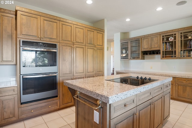 kitchen with a center island, black electric cooktop, double oven, and light tile floors