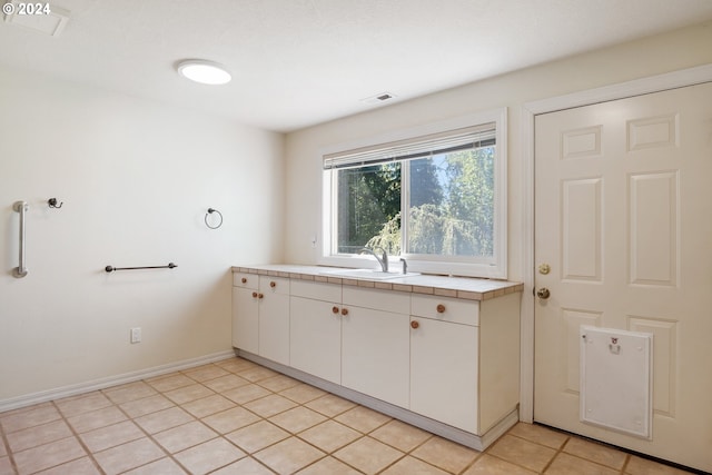 kitchen with tile countertops, sink, light tile floors, and white cabinetry