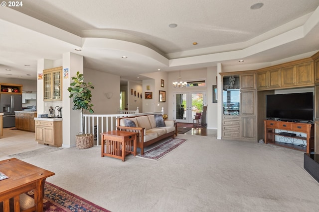 tiled living room with french doors, a tray ceiling, and an inviting chandelier