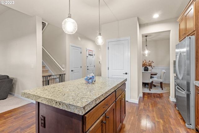 kitchen with stainless steel fridge, a kitchen island, hanging light fixtures, and dark wood-type flooring