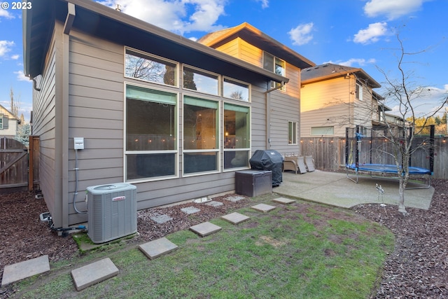 rear view of property featuring a trampoline, a lawn, a patio area, and central air condition unit