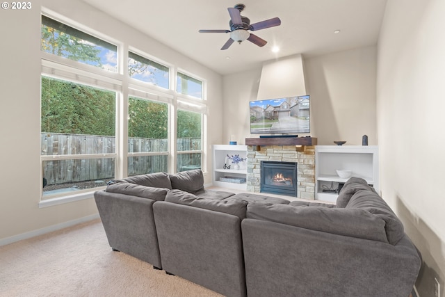 living room with a stone fireplace, ceiling fan, and light colored carpet