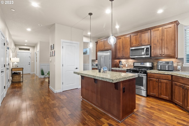 kitchen featuring hanging light fixtures, stainless steel appliances, dark hardwood / wood-style floors, a breakfast bar, and a center island with sink