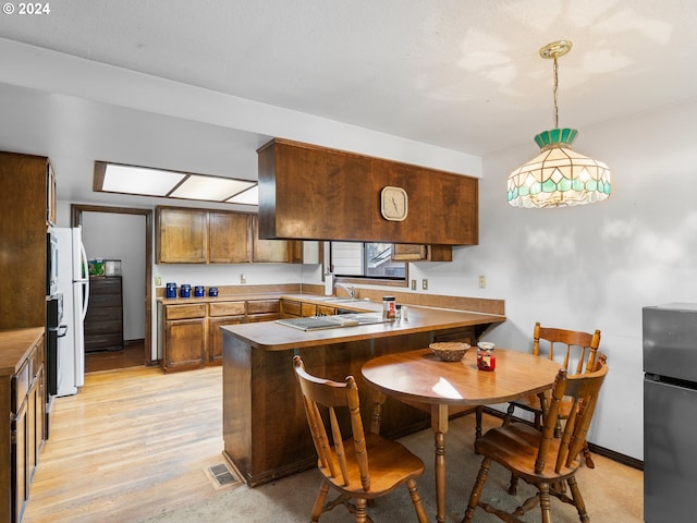 kitchen with hanging light fixtures, kitchen peninsula, stainless steel fridge, light hardwood / wood-style floors, and a breakfast bar area