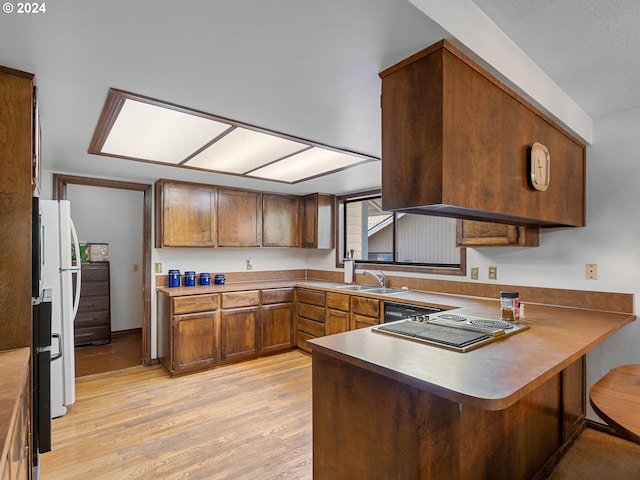 kitchen with sink, kitchen peninsula, white fridge, light hardwood / wood-style floors, and a kitchen bar