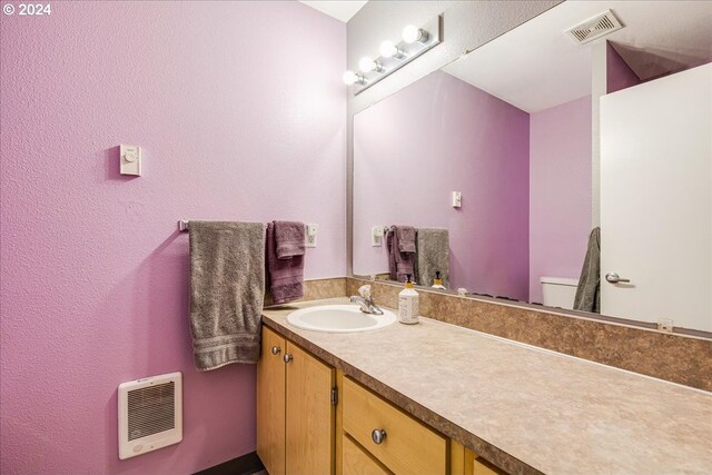 bathroom featuring heating unit, vanity, and toilet