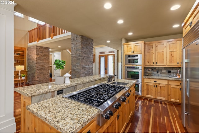 kitchen with ornate columns, a center island, stainless steel appliances, dark wood-type flooring, and light stone counters