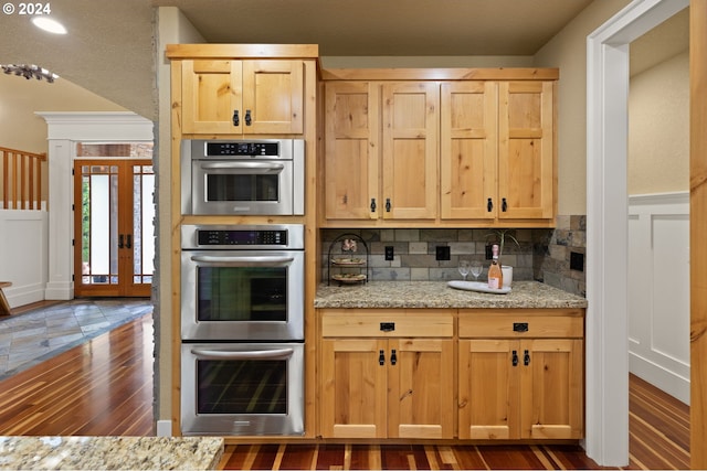 kitchen featuring dark wood-type flooring, light stone countertops, light brown cabinetry, tasteful backsplash, and stainless steel double oven