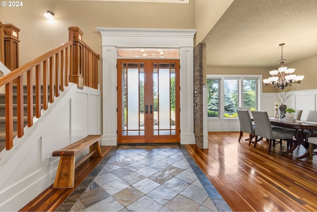 entryway featuring a textured ceiling, a chandelier, dark wood-type flooring, and french doors