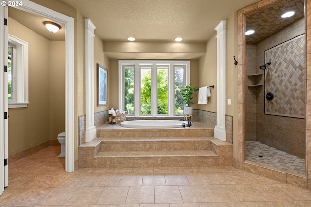 bathroom with tile patterned flooring, decorative columns, a textured ceiling, shower with separate bathtub, and toilet