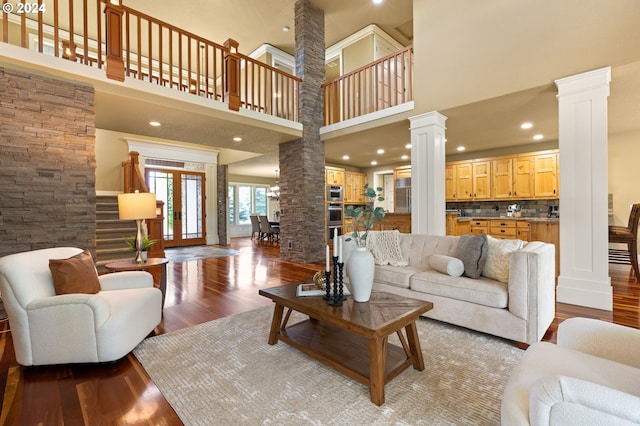 living room with wood-type flooring, a towering ceiling, and ornate columns