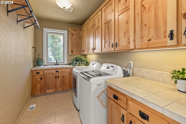 laundry area featuring sink, cabinets, a textured ceiling, washer and clothes dryer, and light tile patterned floors