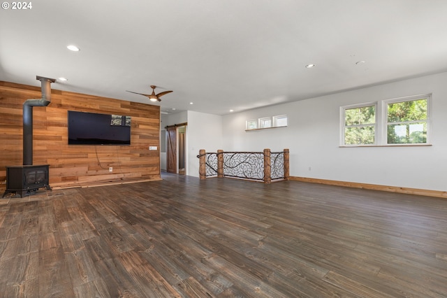 living room featuring dark hardwood / wood-style floors, ceiling fan, a wood stove, and wooden walls