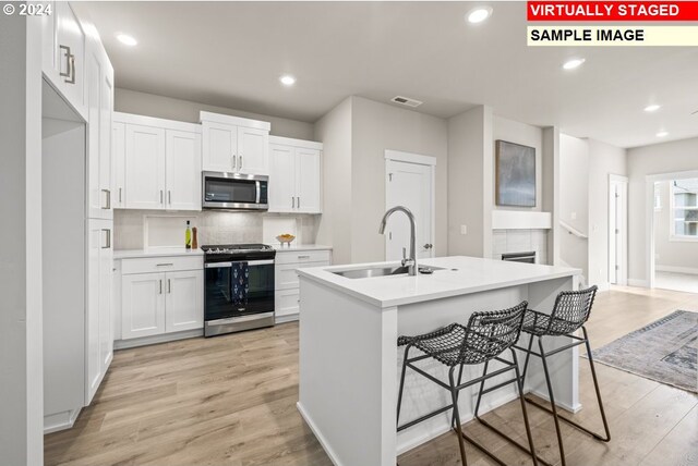 kitchen featuring white cabinets, appliances with stainless steel finishes, a kitchen island with sink, light hardwood / wood-style flooring, and sink