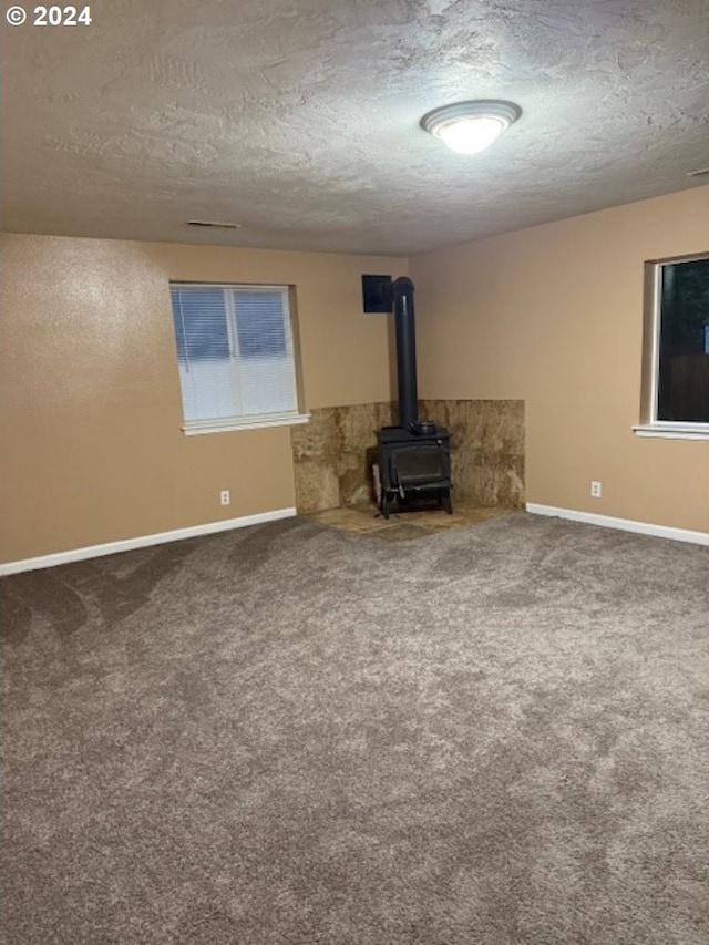 unfurnished living room with a textured ceiling, carpet floors, and a wood stove