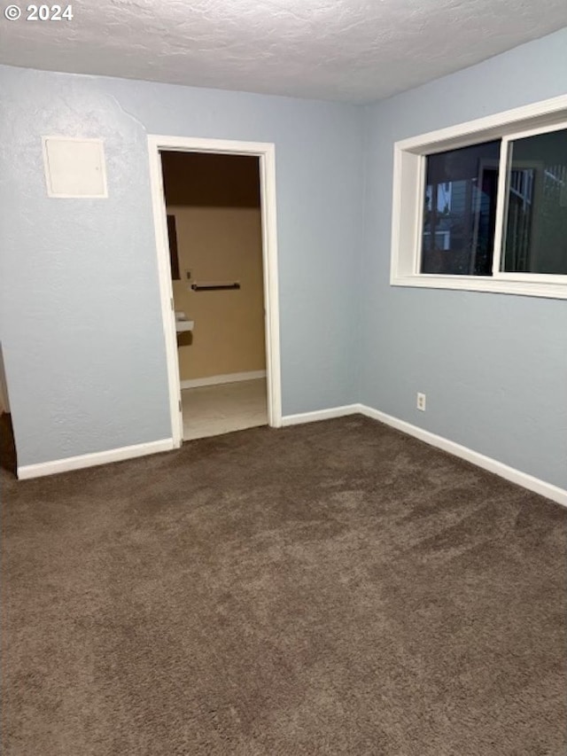 unfurnished room featuring dark colored carpet and a textured ceiling