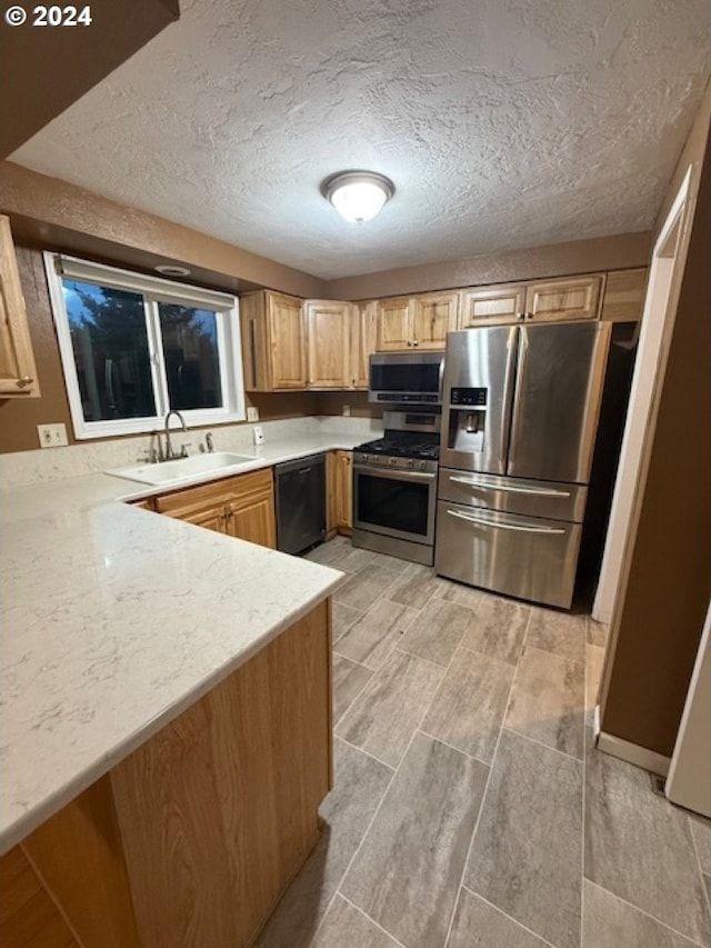 kitchen featuring light brown cabinets, sink, light wood-type flooring, a textured ceiling, and stainless steel appliances