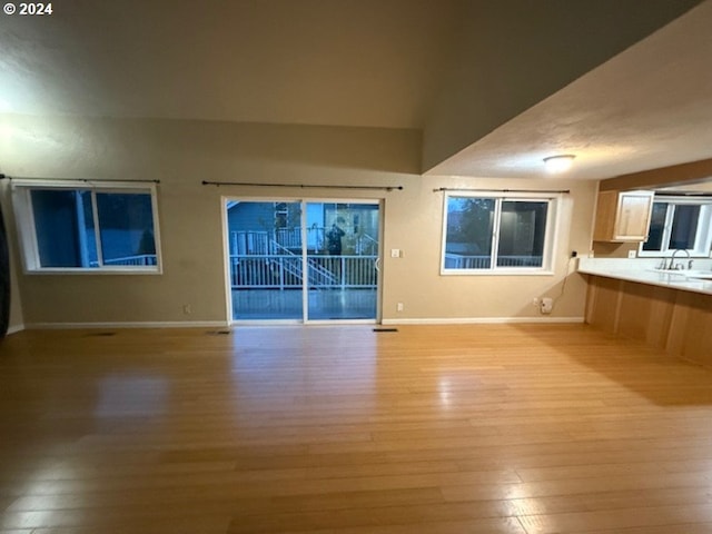 unfurnished living room featuring light hardwood / wood-style flooring, vaulted ceiling, and sink