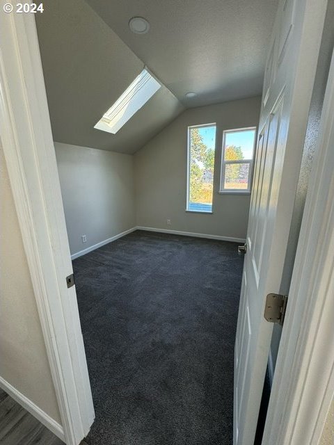 additional living space featuring vaulted ceiling with skylight and dark carpet