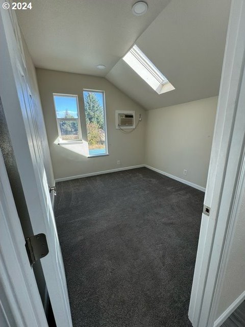 additional living space with a wall unit AC, dark carpet, and vaulted ceiling with skylight