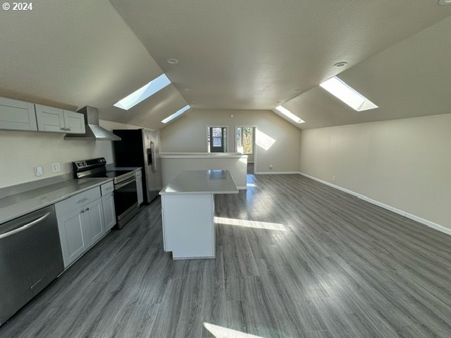 kitchen featuring white cabinets, a center island, lofted ceiling with skylight, and appliances with stainless steel finishes