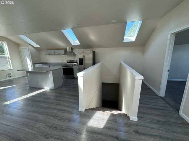 kitchen featuring a center island, wall chimney exhaust hood, dark wood-type flooring, lofted ceiling with skylight, and appliances with stainless steel finishes