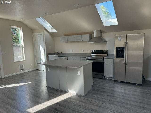 kitchen with wall chimney exhaust hood, stainless steel appliances, dark hardwood / wood-style flooring, lofted ceiling with skylight, and a kitchen island