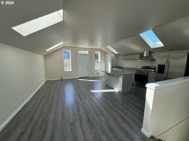 kitchen with dark wood-type flooring, wall chimney range hood, lofted ceiling, a kitchen island, and appliances with stainless steel finishes