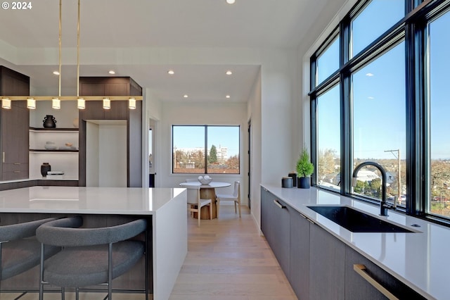 kitchen featuring gray cabinetry, a breakfast bar, sink, light hardwood / wood-style floors, and hanging light fixtures