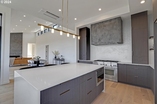 kitchen featuring wall chimney range hood, light hardwood / wood-style flooring, a towering ceiling, a large island, and stainless steel appliances