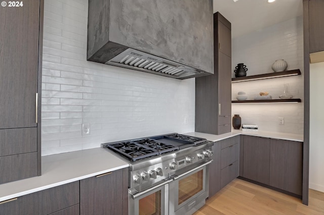 kitchen with light wood-type flooring, high end stove, backsplash, and wall chimney range hood