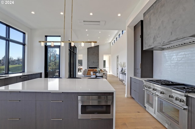 kitchen featuring decorative backsplash, a spacious island, decorative light fixtures, light hardwood / wood-style flooring, and double oven range