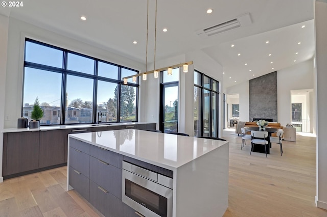 kitchen with sink, light hardwood / wood-style flooring, a fireplace, a center island, and stainless steel microwave