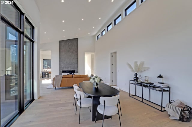 dining space featuring a fireplace, a towering ceiling, and light hardwood / wood-style flooring